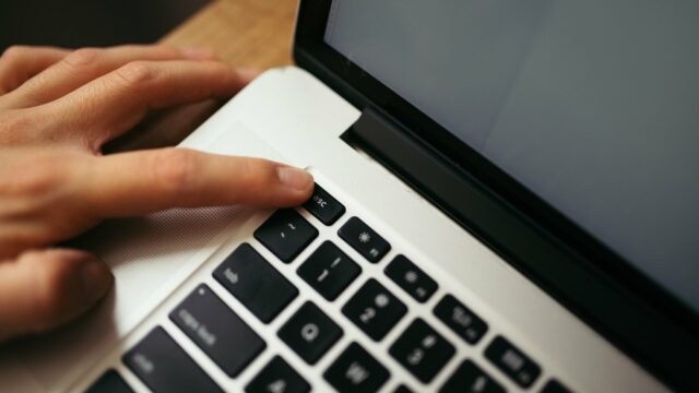 Jak zadawać dobre pytania AI — prompty bez tajemnic — A hand rests on a laptop keyboard, pressing a key.jpg